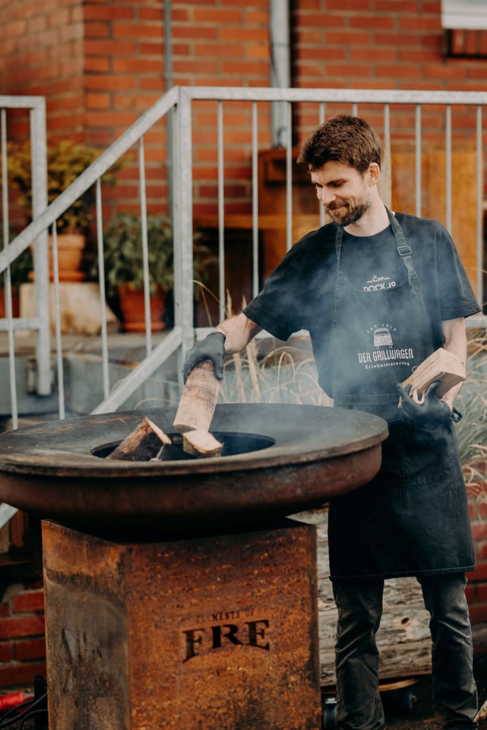 Mitarbeiter des Grillwagens legt Holz in die Feuerplatte nach