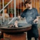 Mitarbeiter des Grillwagens legt Holz in die Feuerplatte nach