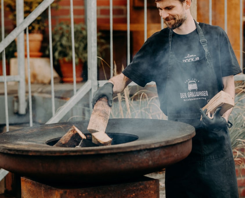 Mitarbeiter des Grillwagens legt Holz in die Feuerplatte nach